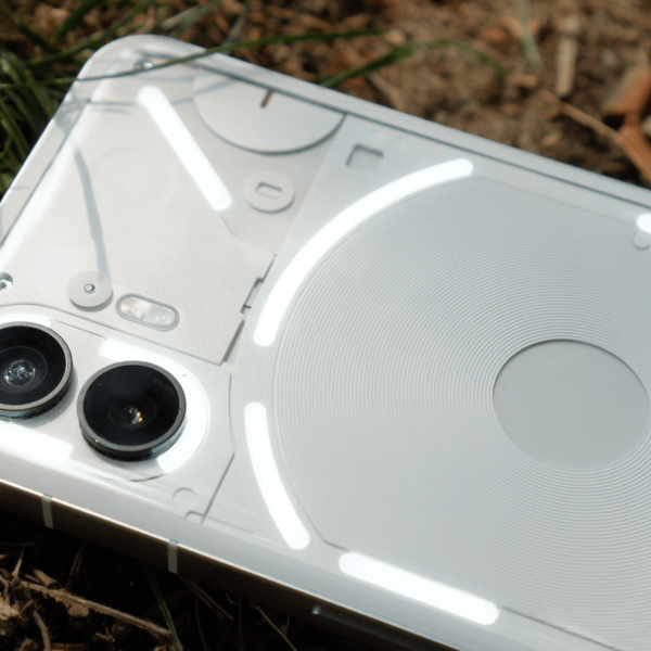 Should you buy the Nothing Phone (2) in 2024? A close-up of the Nothing Phone (2) lying on a bed of grass and soil, showcasing its dual-camera system and internal components illuminated by natural light.