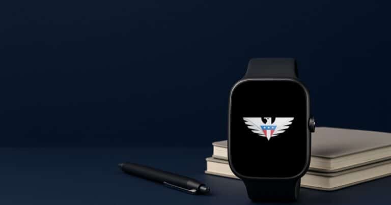 A smartwatch with the us mobile eagle on its screen beside a stack of notebooks and a pen