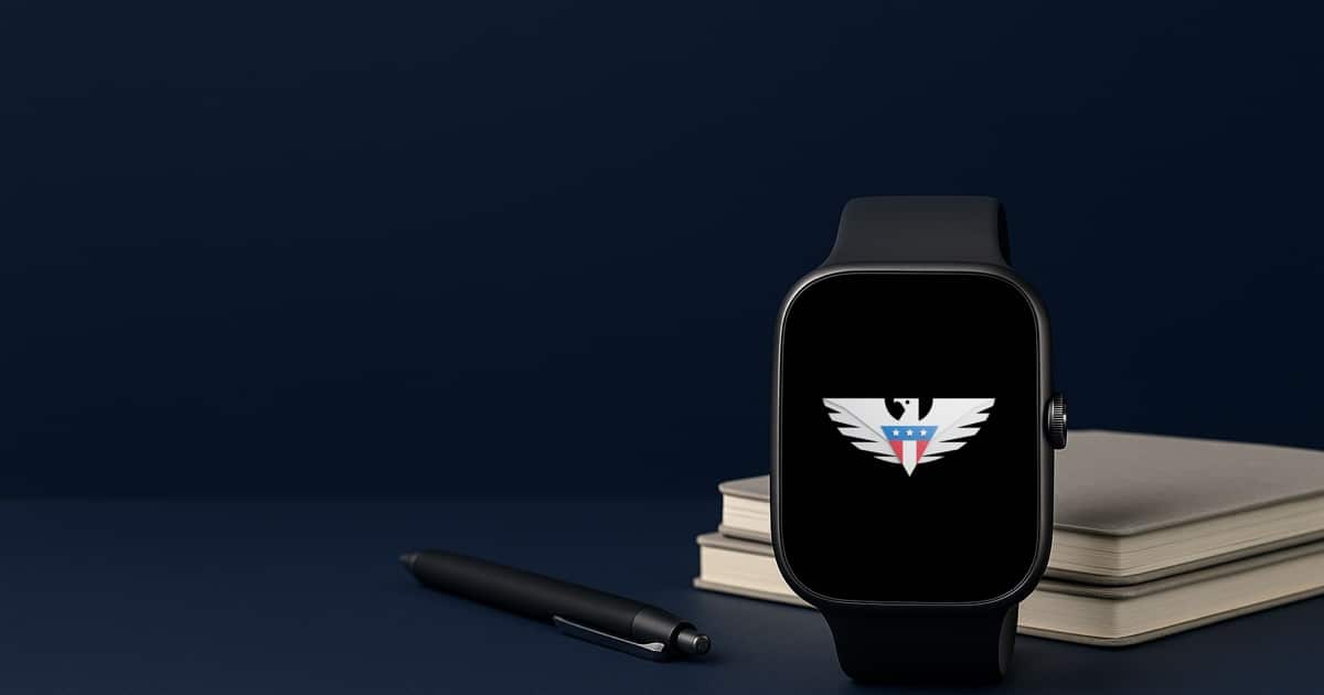 A smartwatch with the us mobile eagle on its screen beside a stack of notebooks and a pen